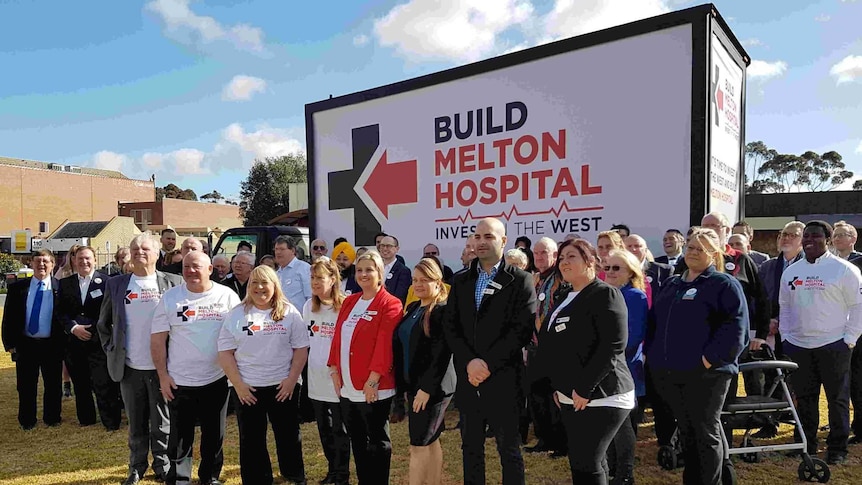 Campaigners pose in front of a Build Melton Hospital billboard.