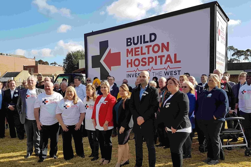 Campaigners pose in front of a Build Melton Hospital billboard.