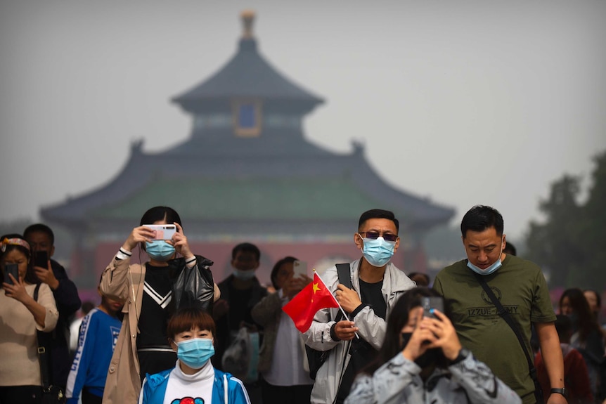 People wearing face masks to protect against the coronavirus at the Temple of Heaven in Beijing, which is blurred in background.