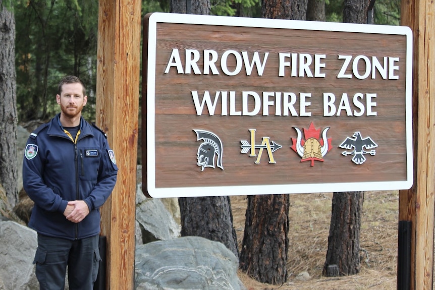 James Koens stands in his RFS uniform next to a sign saying Arrow Fire Zone Wildfire Base.