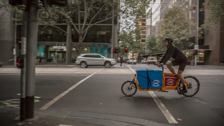 A man riding a cargo bike - a bike with an extended frame and a large blue box built into it