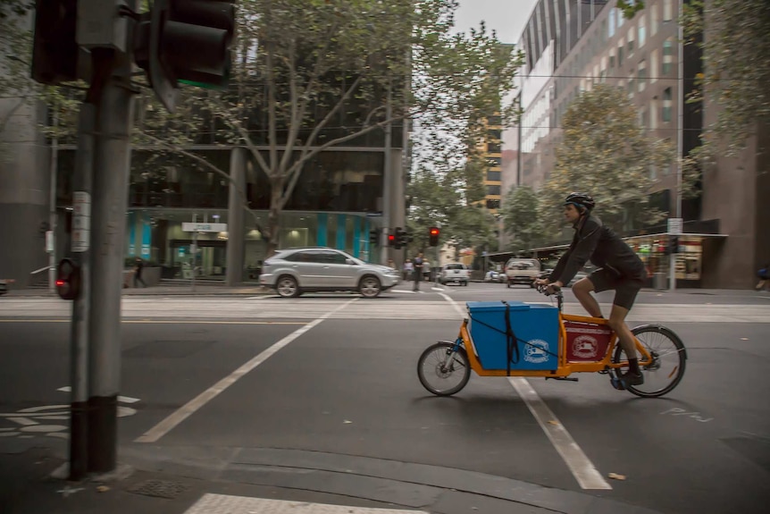 A man riding a cargo bike - a bike with an extended frame and a large blue box built into it