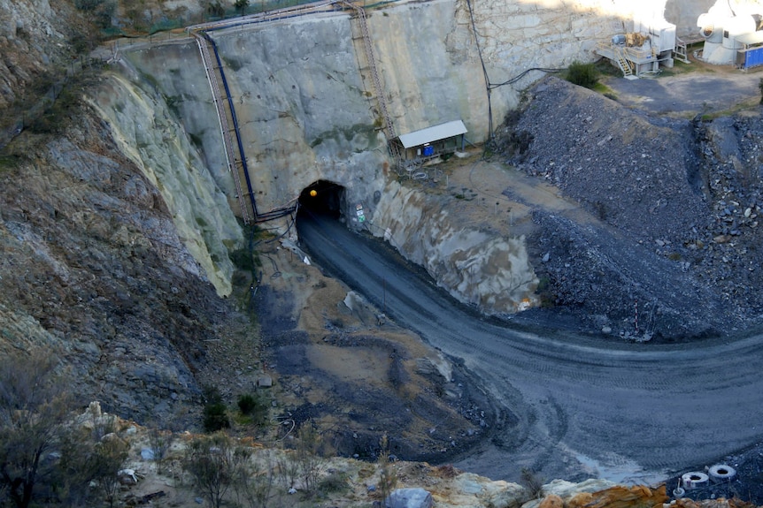 A road leads into the mouth of a cave cut into the side of the open cut mine
