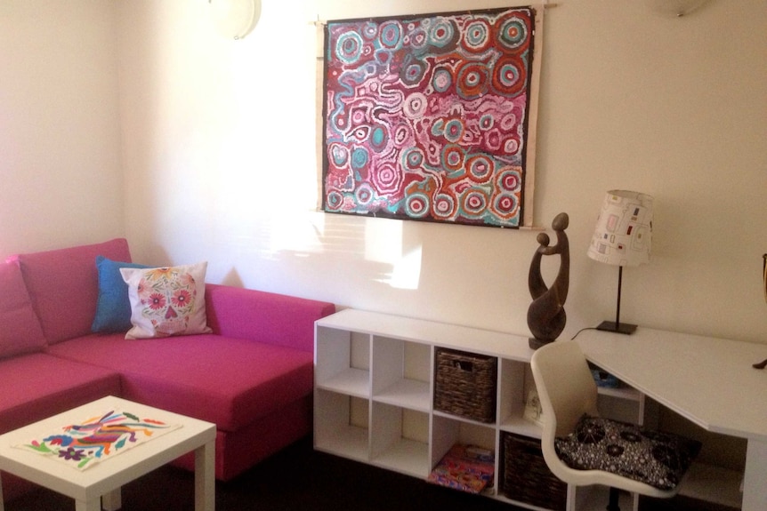 A living room furnished with fast furniture, including a bright pink couch and Indigenous artwork on the wall.