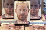 Multiple copies of the book Spare at a bookshop, some front facing, others underneath. Prince Harry is on the cover