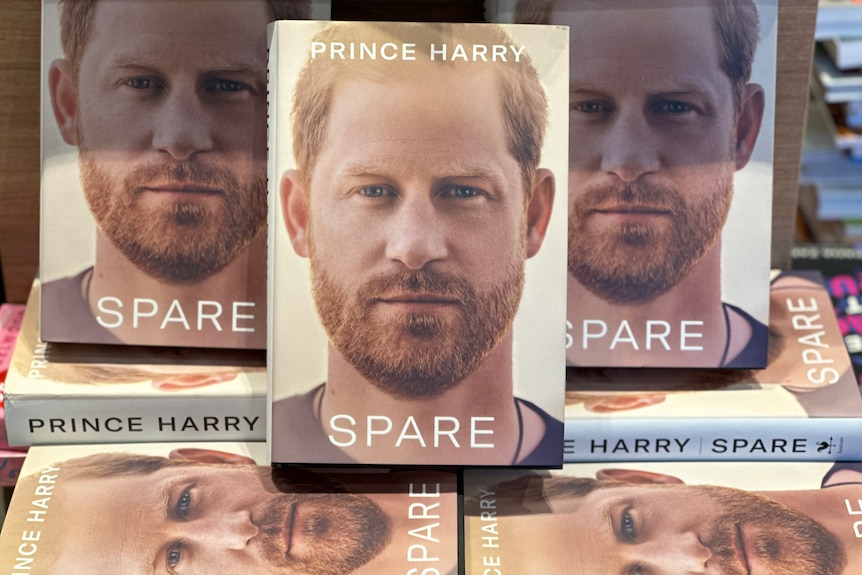 Multiple copies of the book Spare at a bookshop, some front facing, others underneath. Prince Harry is on the cover