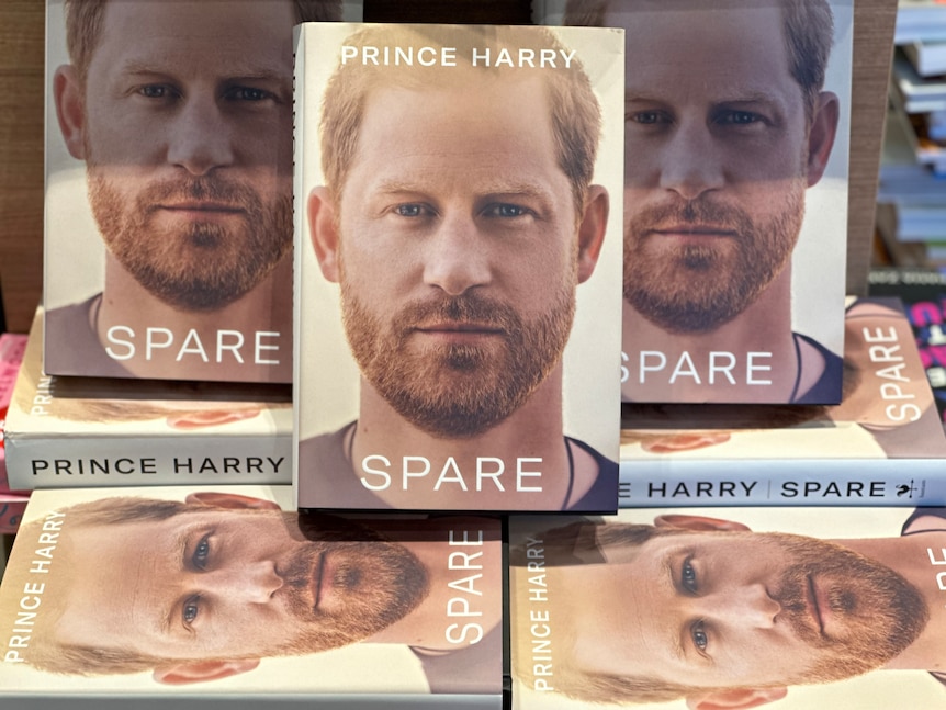Multiple copies of the book Spare at a bookshop, some front facing, others underneath. Prince Harry is on the cover