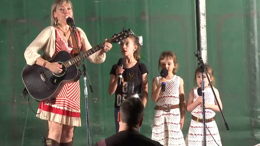 Felicity Urquhart and three young girls sing together on stage.