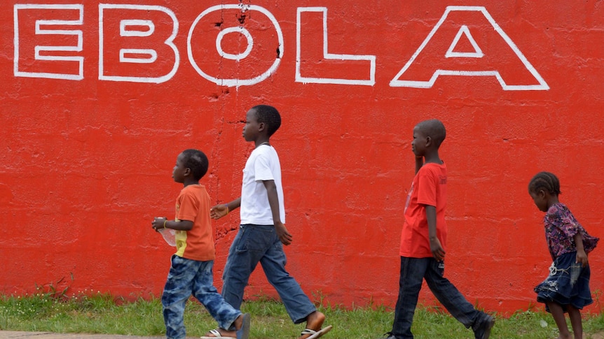 Children walk past a slogan painted in Monrovia