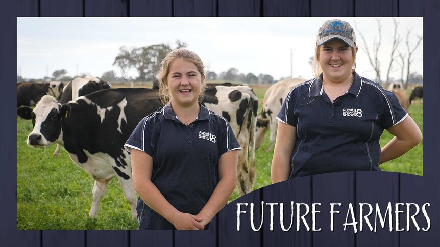 Two teenage girls smile while standing in front of dairy cows