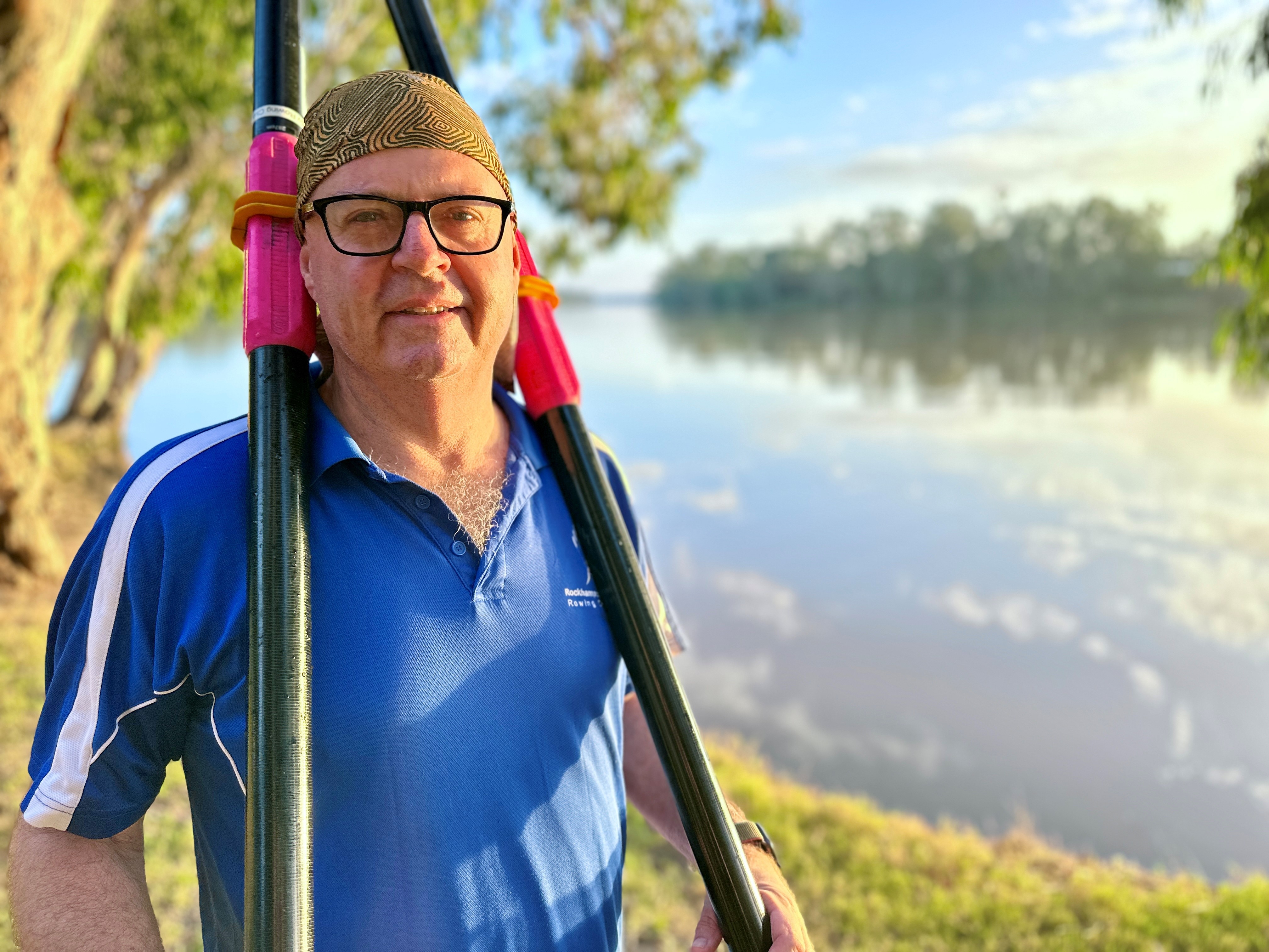 A man holds two oars next to a river.