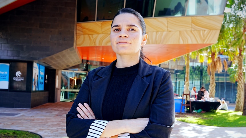 Woman with dark brown hair and black blazer standing in front of building