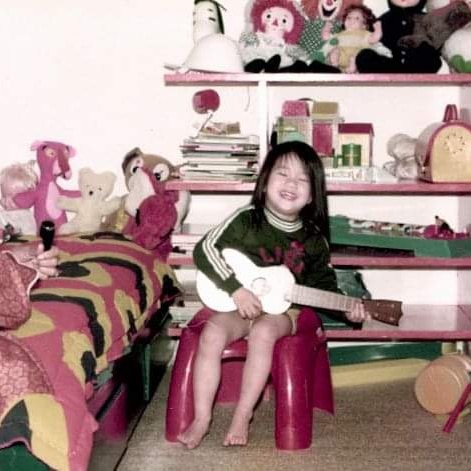 Lisa Leong as a child playing the guitar in her bedroom smiling