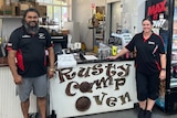 Two staff stand outside of a cafe sign 
