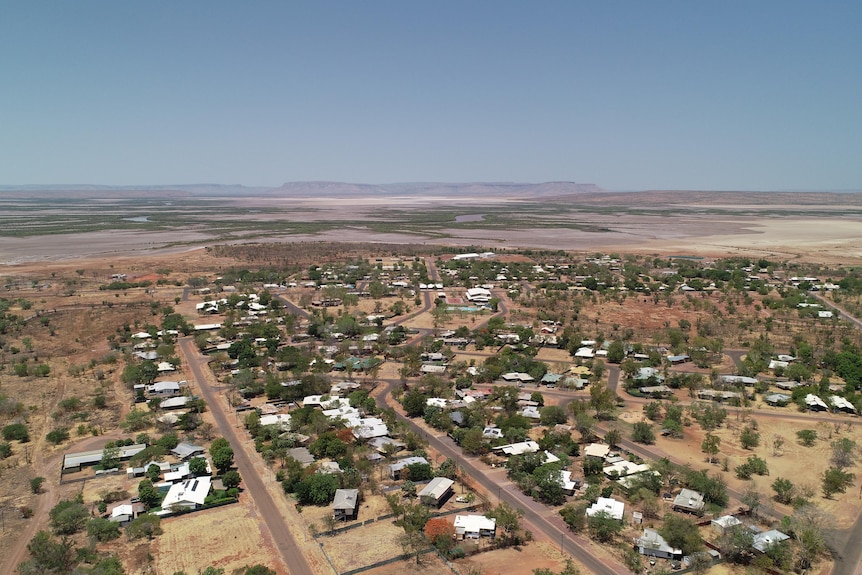 Aerial photo of outback town with salt pans and ranges in the distance.