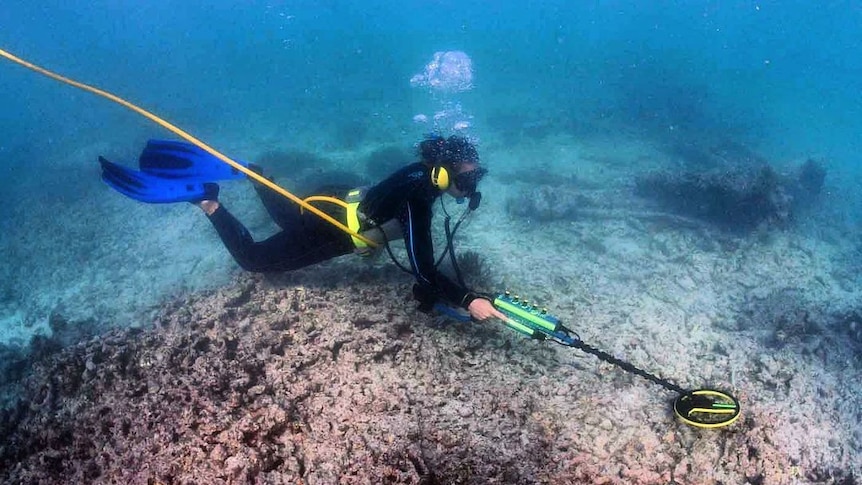 A woman diving in the ocean with a mental detector