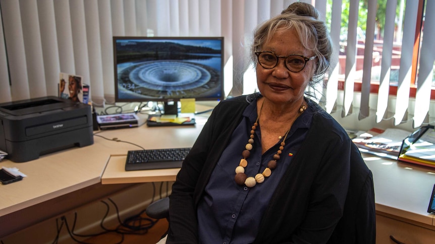 An older Indigenous woman in dark clothes sitting in an office.