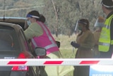 Woman wearing yellow safety suit and pink hi vis vest leans into a car window.
