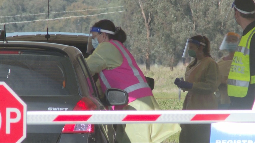 Woman wearing yellow safety suit and pink hi vis vest leans into a car window.