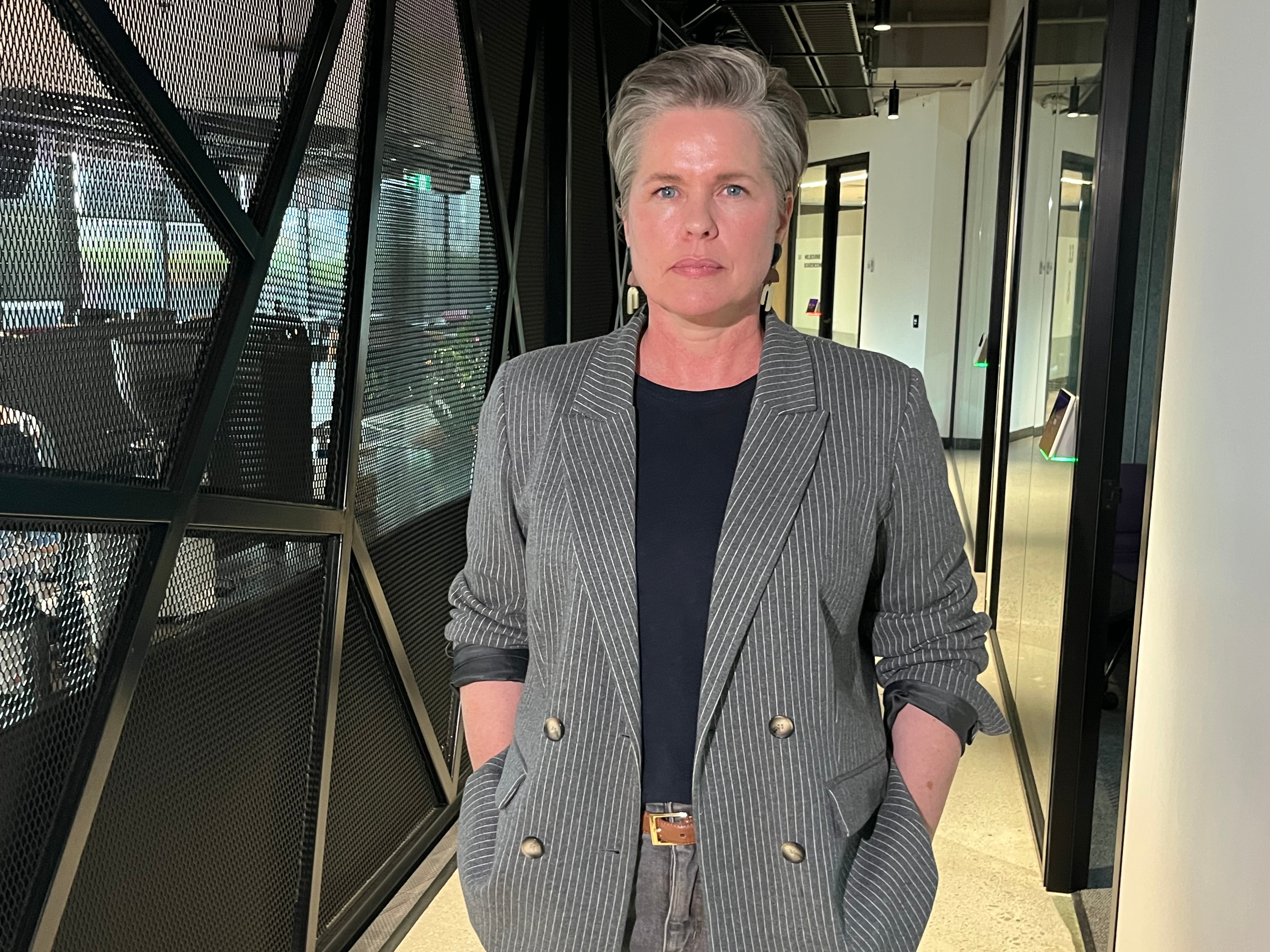 Woman with short hair and blazer looks at camera while standing in office space