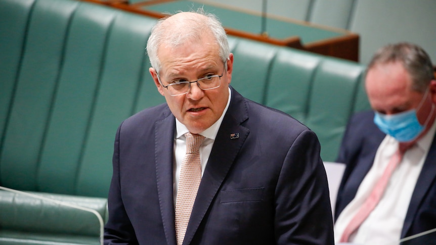 Morrison has a concerned expression, standing up in the a dark suit and light tie.