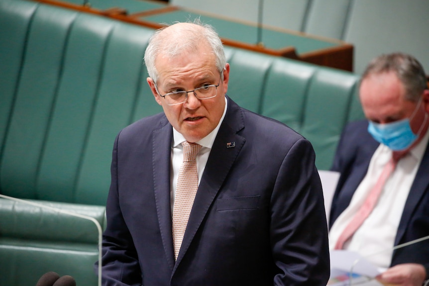 Morrison has a concerned expression, standing up in the a dark suit and light tie.