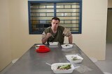 ABC reporter Tim Swanston sitting at a table in prison eating food