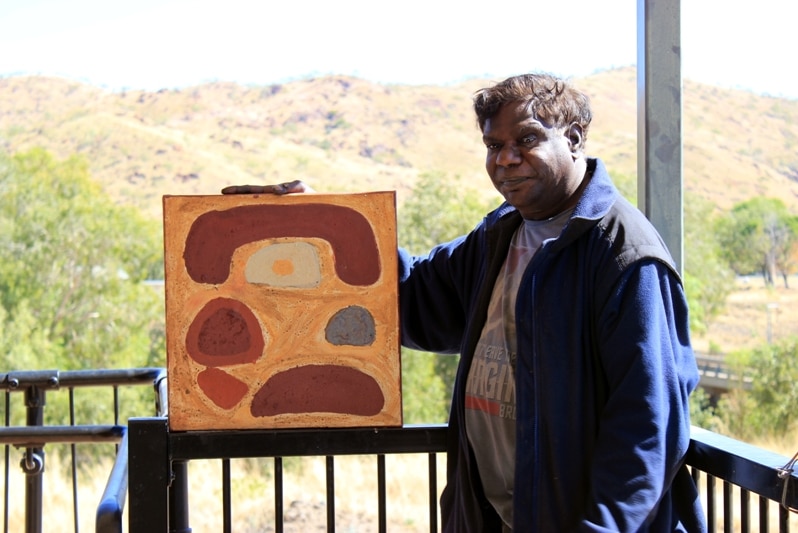 A man standing on a balcony is holding a piece of artwork.