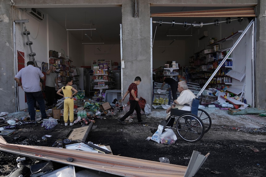 people walk among damaged goods in front of a damaged storefront