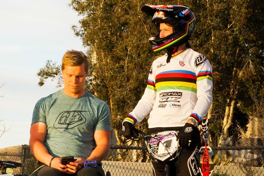 Sam Willoughby sits in a wheelchair next to his wife Alise who is standing over a BMX