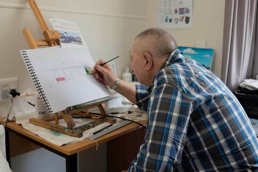 Elderly man painting on a small easel. 