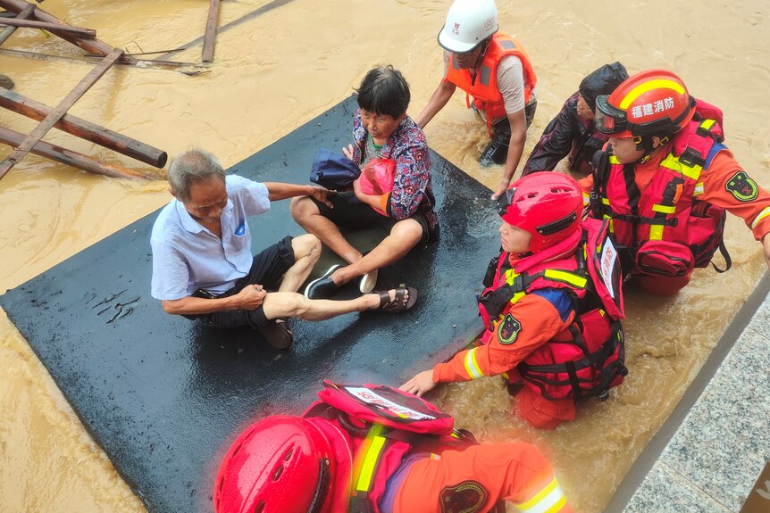 Rescue workers float and elderly couple on a mat in floodwaters. 