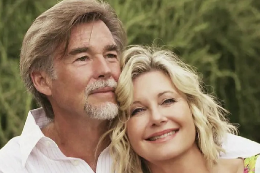 John Easterling and Olivia Newton-John smile together outdoors.