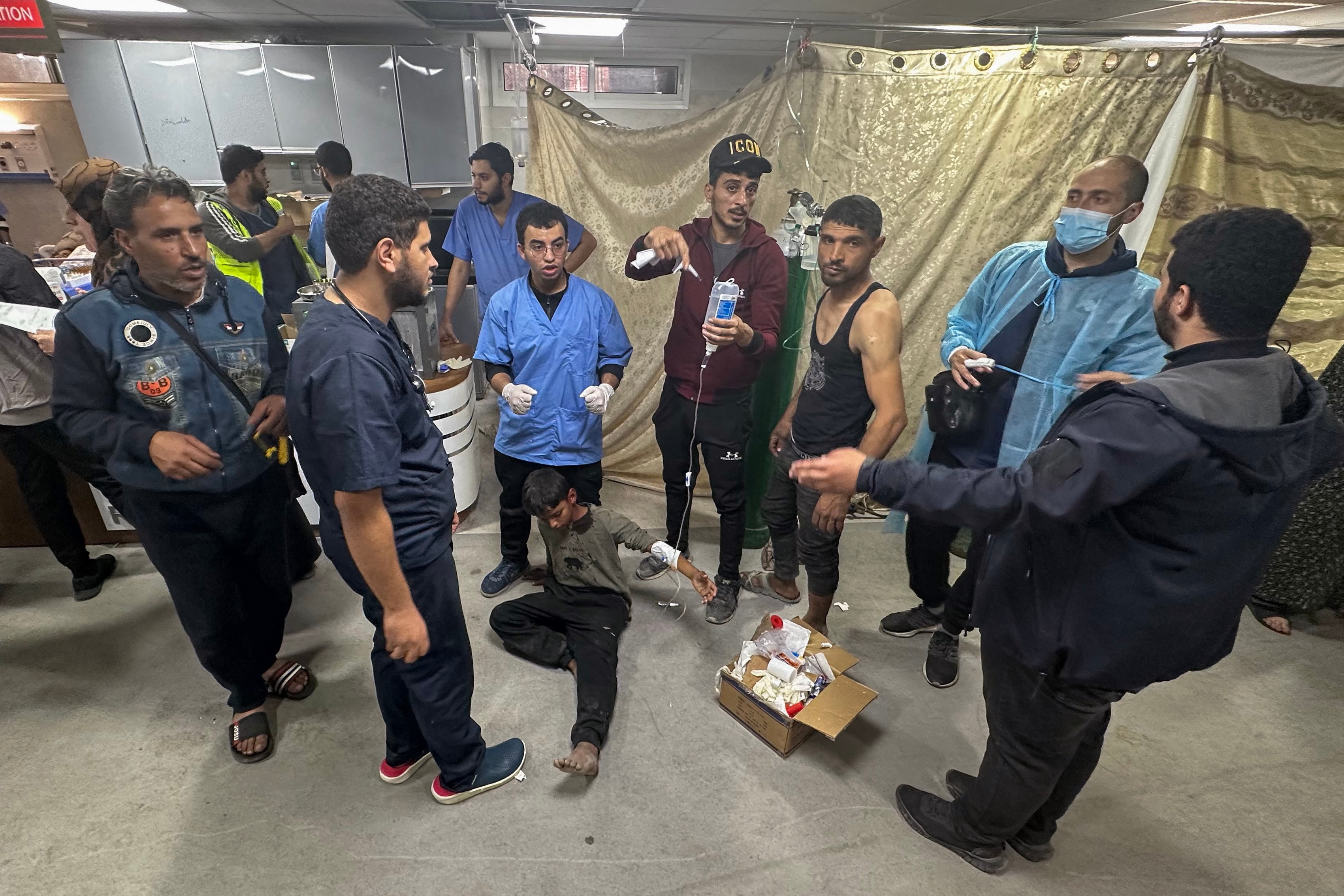 medics stand around as a boy sits on the ground with an IV drip attached, one man holding up the bag