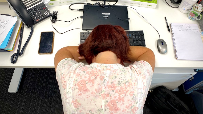 A woman sitting at office work station with her head on the desk.