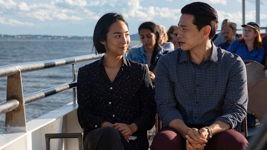 Actors Greta Lee and Teo Yoo sit on a ferry in the film Past Lives.