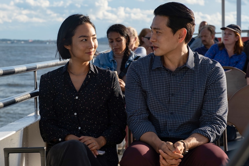 Actors Greta Lee and Teo Yoo sit on a ferry in the film Past Lives.
