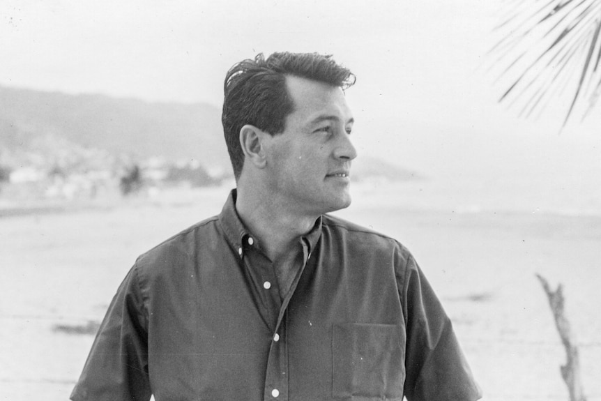 Black and white image of Rock Hudson, he is wearing a dark coloured shirt. He is looking to the right in the picture. 