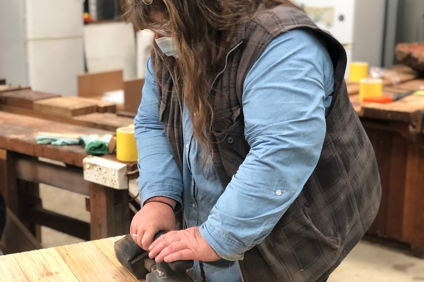 Woman using an electric sander on a woodworking project in a workshop