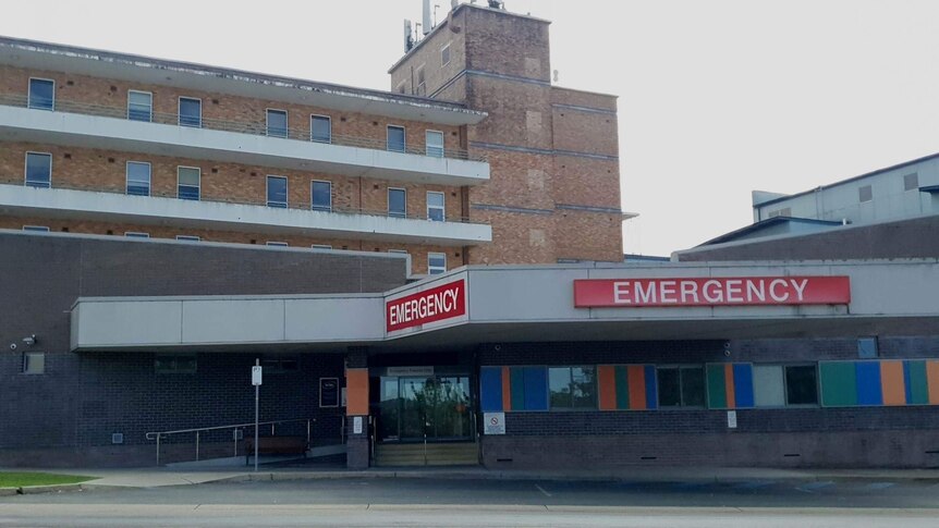 The outside of the hospital building, with a red emergency sign at the front.