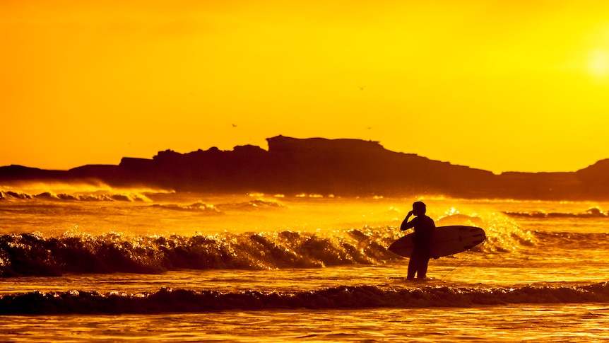 An orange-tinged image shows the silhouette of a man with a surfboard standing in the surf.