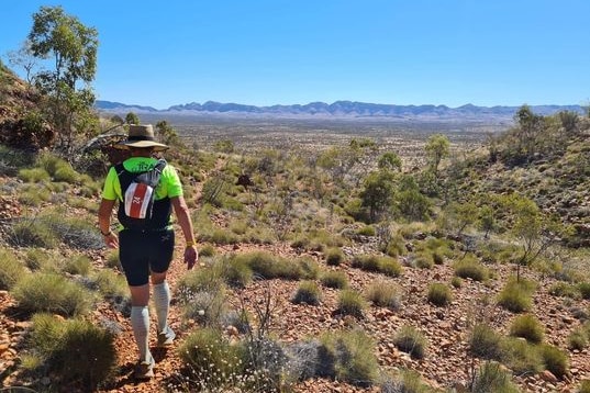 woman with back to camera in the middle of the desert with rocky outcrop in distance