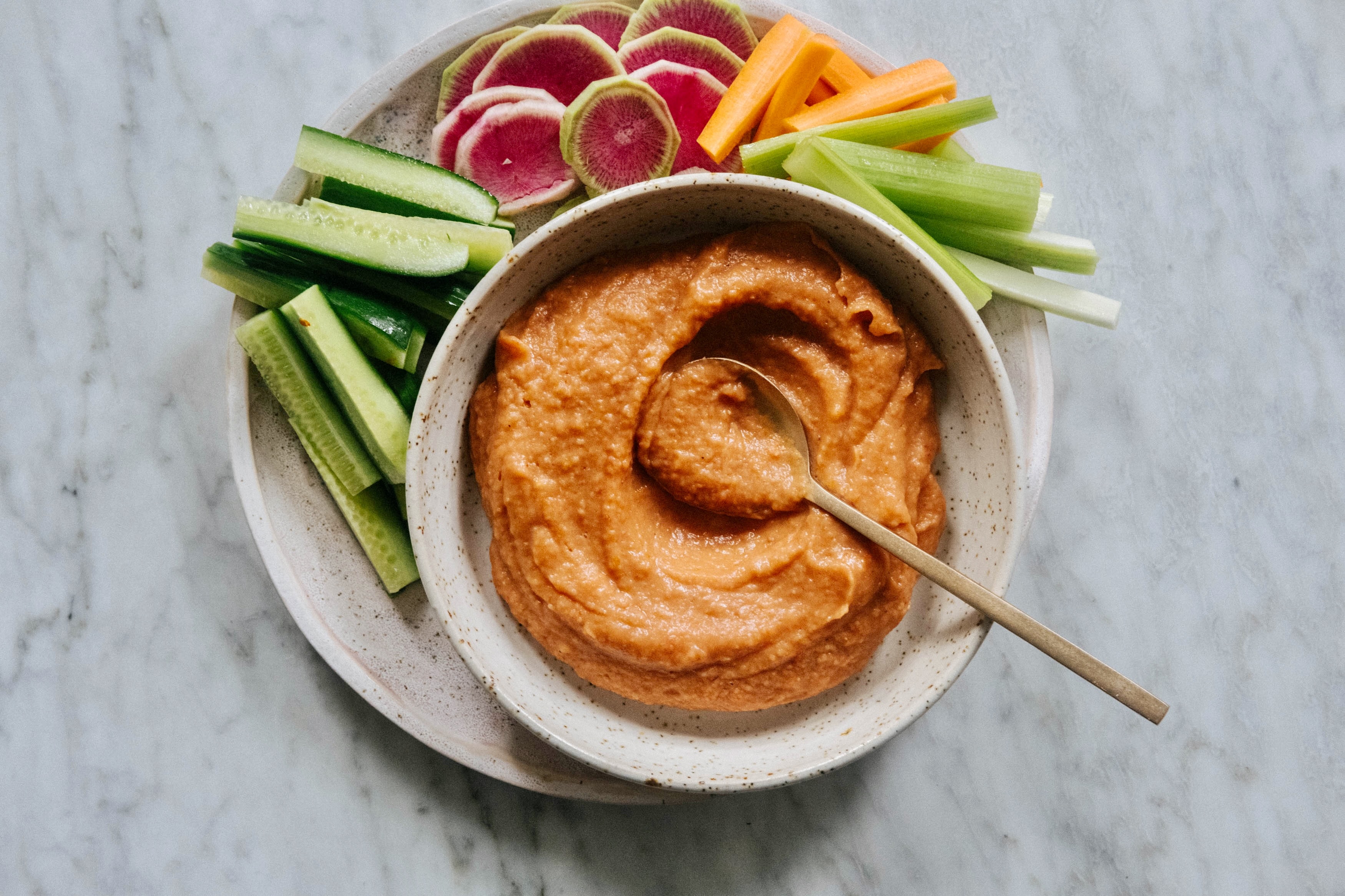 An aerial view of a bowl of dip, with sliced cucumbers, celery and carrot bordering it