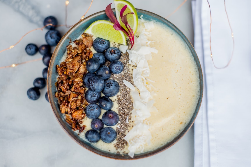 A bowl holding blueberries, cereal and seeds.