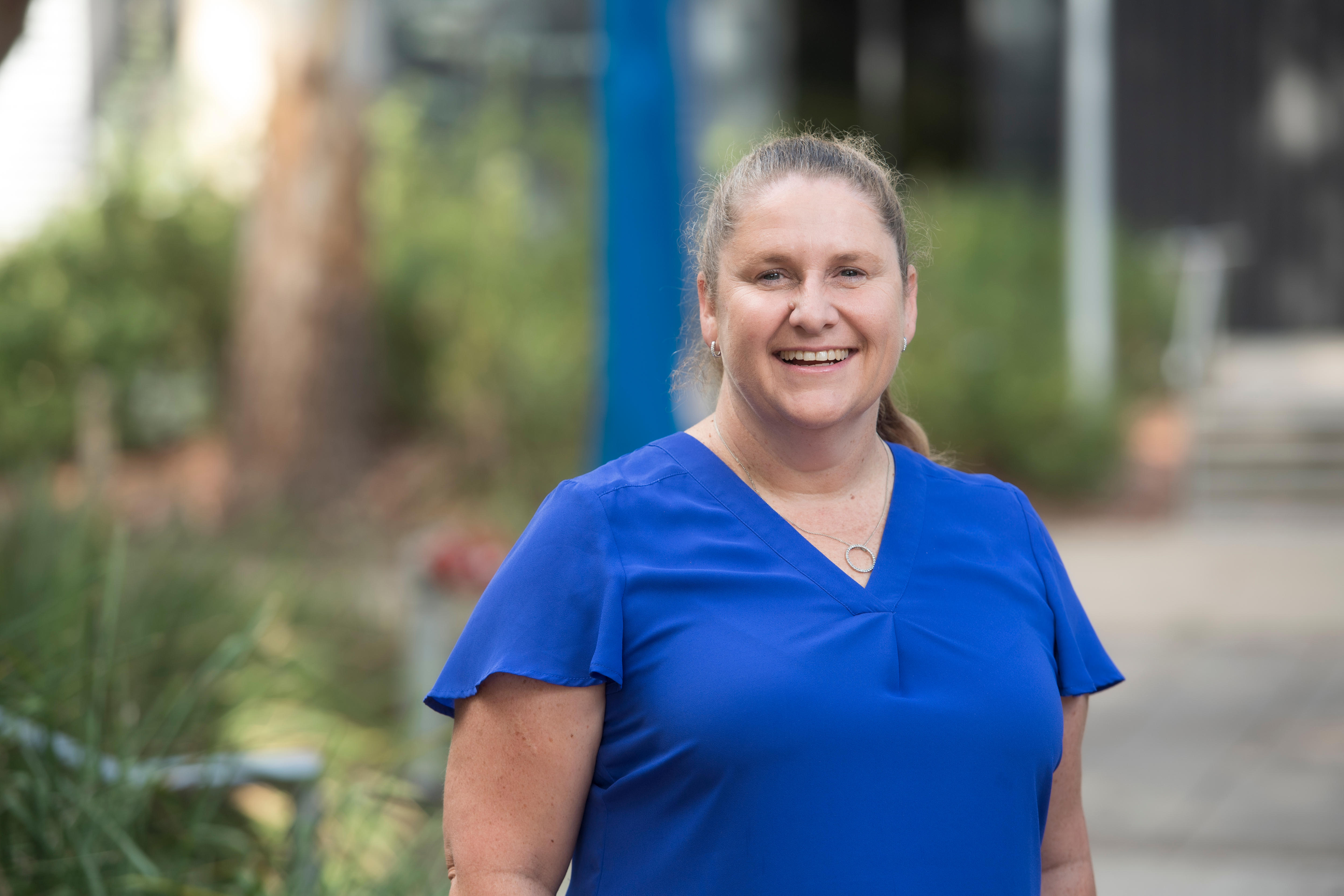 Mulher vestindo camisa azul do lado de fora sorrindo para a câmera 