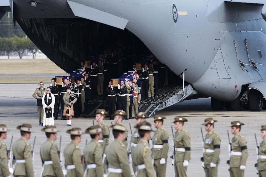 Australian Defence Force personnel carry coffins down the ramp of a C-17 Globemaster III.