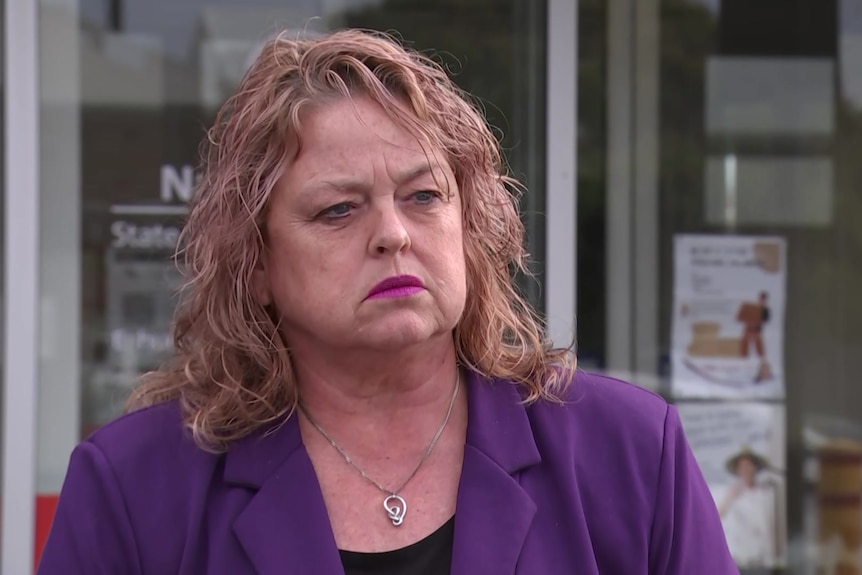 A woman wearing a purple blazer and purple lipstick with a serious expression