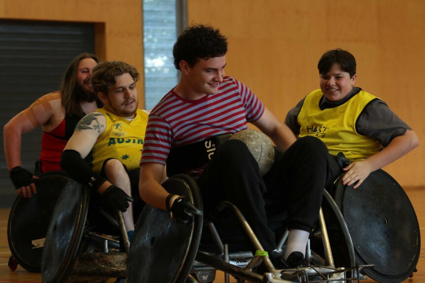 Four men in wheelchairs, one in a red stripy shirt and two behind him wearing yellow bibs.