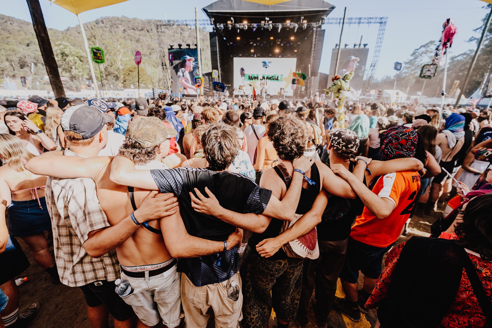 Six men stand at the back of a live gig crowd with their arms over each others shoulders