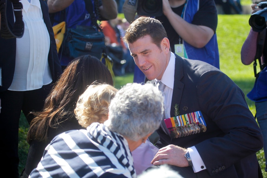 a man with medals on his lapel kneels down to talk to a group of people